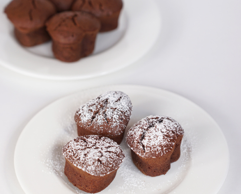 drei Muffins mit Schokolade und Nougat auf weißem Teller, mit Puderzucker bestäubt