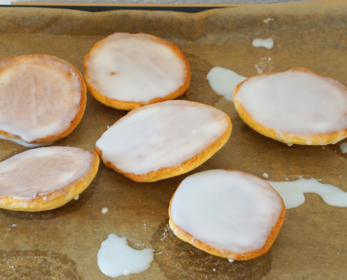 sechs Amerikaner frisch mit Zuckerglasur überzogen auf einem Blech mit Backpapier