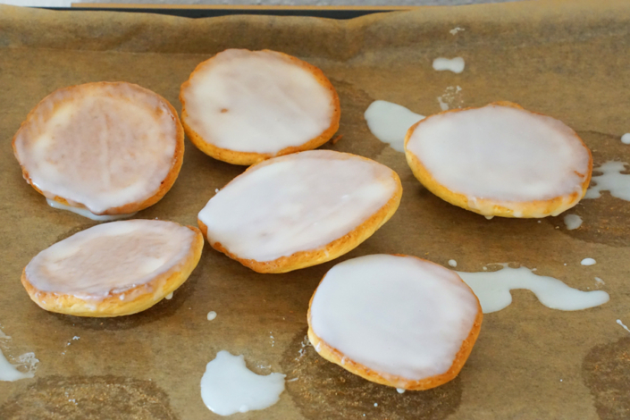 sechs Amerikaner frisch mit Zuckerglasur überzogen auf einem Blech mit Backpapier