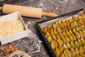 Küchenarbeitsplatte mit Backblech, belegt mit Hefeteig und Zwetschgen, daneben Rollholz und Teigstreusel in Schale