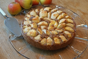 Apfelkuchen mit Nussboden, frisch gebacken auf gläsernen Tortenplatte