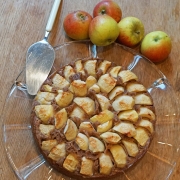 Apfelkuchen auf Tortenplatte, am Rand liegen frische Äpfel