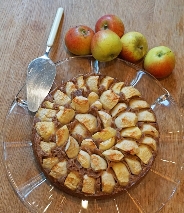 Apfelkuchen auf Tortenplatte, am Rand liegen frische Äpfel